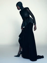 Model Ajok Madel wears an all-black hooded silhouette gown with pointed stiletto heels against a pale studio backdrop.