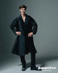 Model Kit Butler wearing a dark long coat against a grey studio backdrop for Esquire Germany editorial.