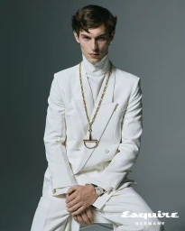 Kit Butler in a white double-breasted suit and gold chain necklace against a grey seamless background for Esquire Germany