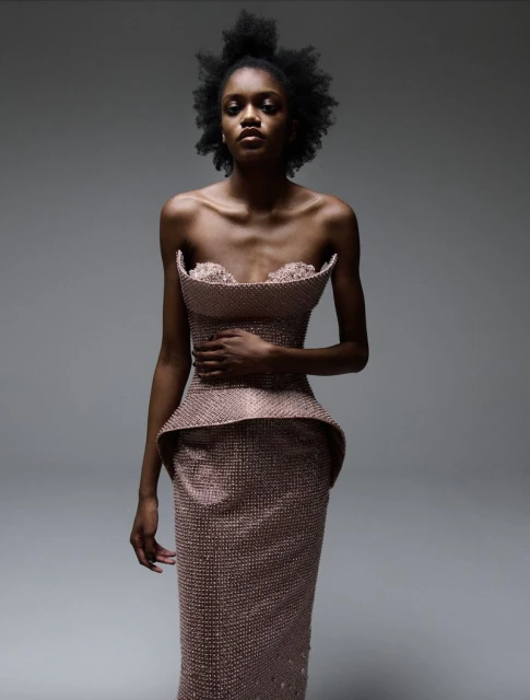 Elegant Black model in strapless embellished dress posing in a photo studio against a grey backdrop for a fashion editorial shot.
