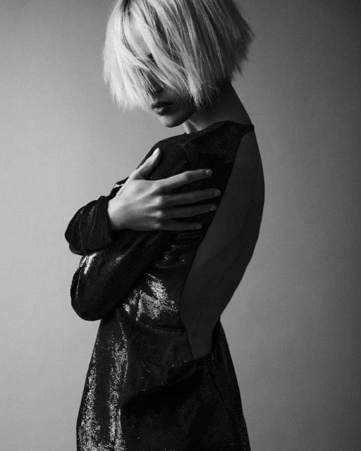 Black and white studio shot of a young adult female with blonde hair, wearing a sparkling black dress, with her arms crossed.