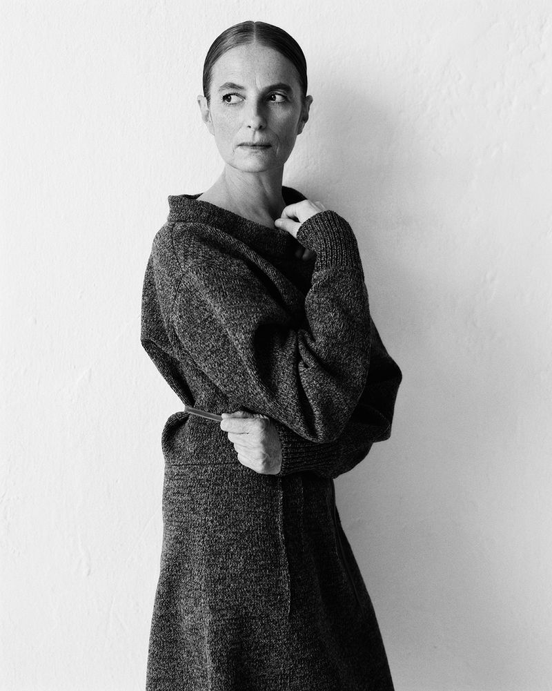 Monochrome portrait of an adult woman in a textured knit dress, gazing to the side, against a neutral white wall backdrop in studio lighting.