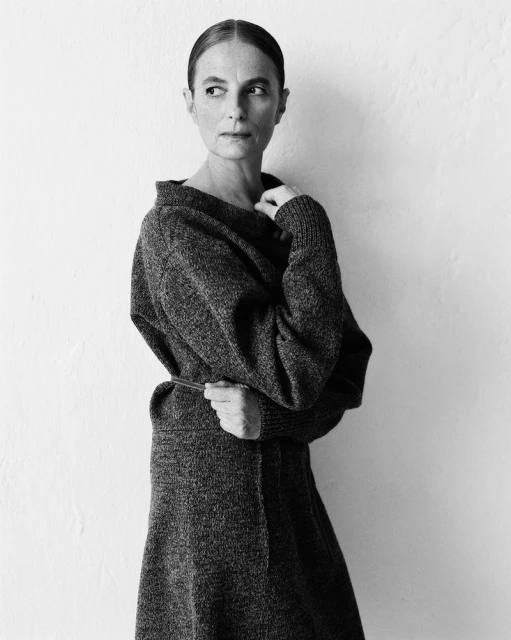 Monochrome portrait of an adult woman in a textured knit dress, gazing to the side, against a neutral white wall backdrop in studio lighting.