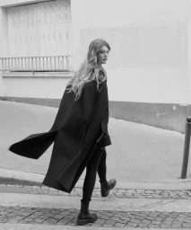 A long dark coat worn by a model walking on a cobblestone street, shot by Indigo Lewin for ICICLE.