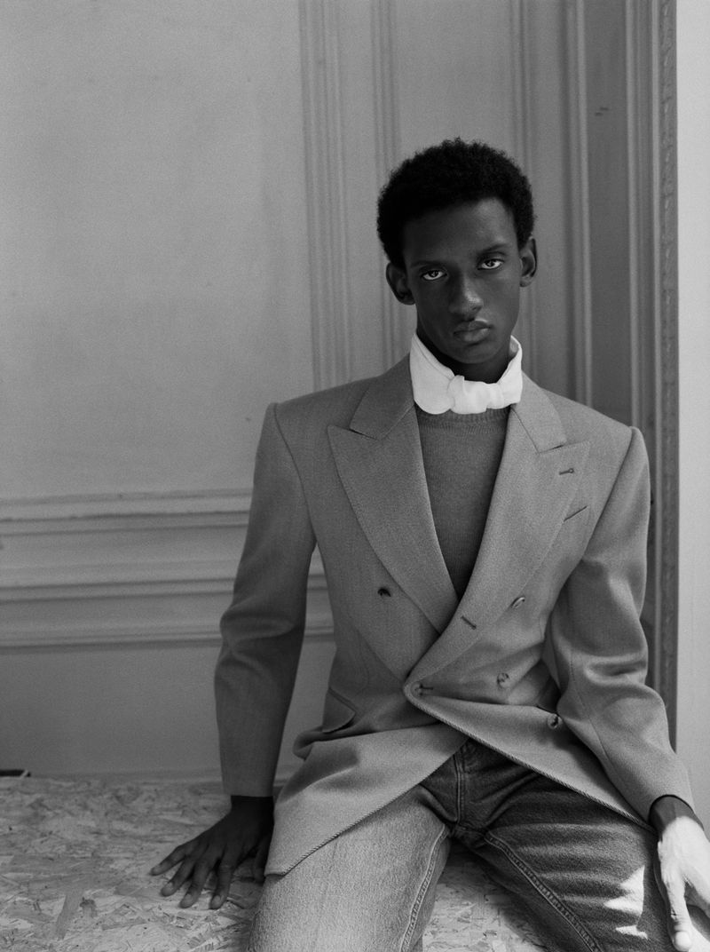 Black and white portrait of an African American man wearing a gray suit and jeans, sitting and looking directly at the camera.