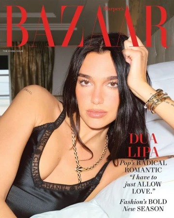 Close-up magazine cover featuring Dua Lipa with dark hair, gold jewelry, black top, resting on a white surface, Harper's Bazaar.