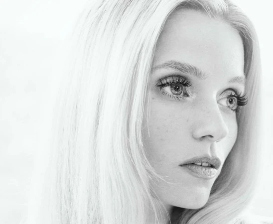 Monochromatic portrait of a fair-skinned adult woman with long blonde hair, looking off to the side against a blurred background.