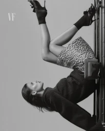 Model wearing a patterned skirt and dark sweater with heels against a plain studio background for Vanity Fair Italia.