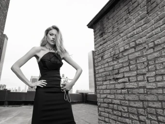 Model Martha Hunt in a black strapless gown standing on a rooftop against a brick wall for L'Officiel Monaco.