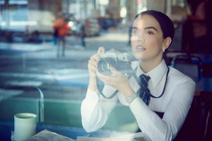 Zoey Deutch holding a vintage camera while seated in a diner for Vanity Fair U.S. captured by Matthew Brookes