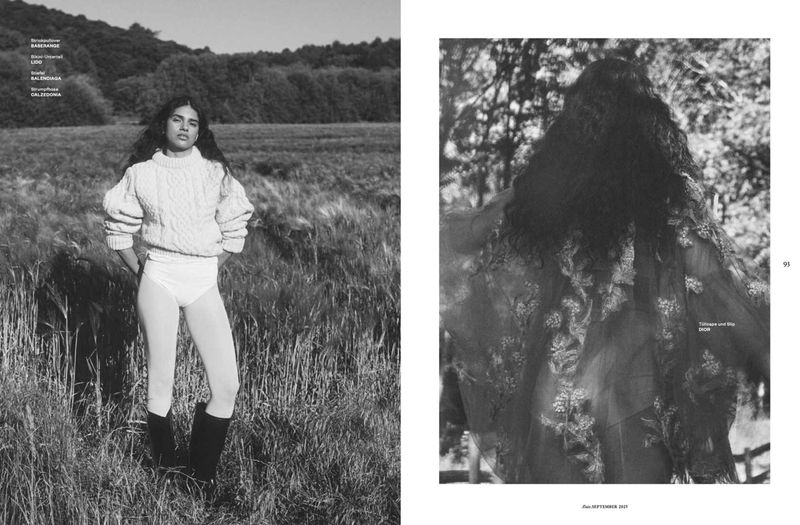 Black and white editorial fashion shot of a young adult woman posing in an open field with knee-high boots, a cable knit sweater, and briefs.