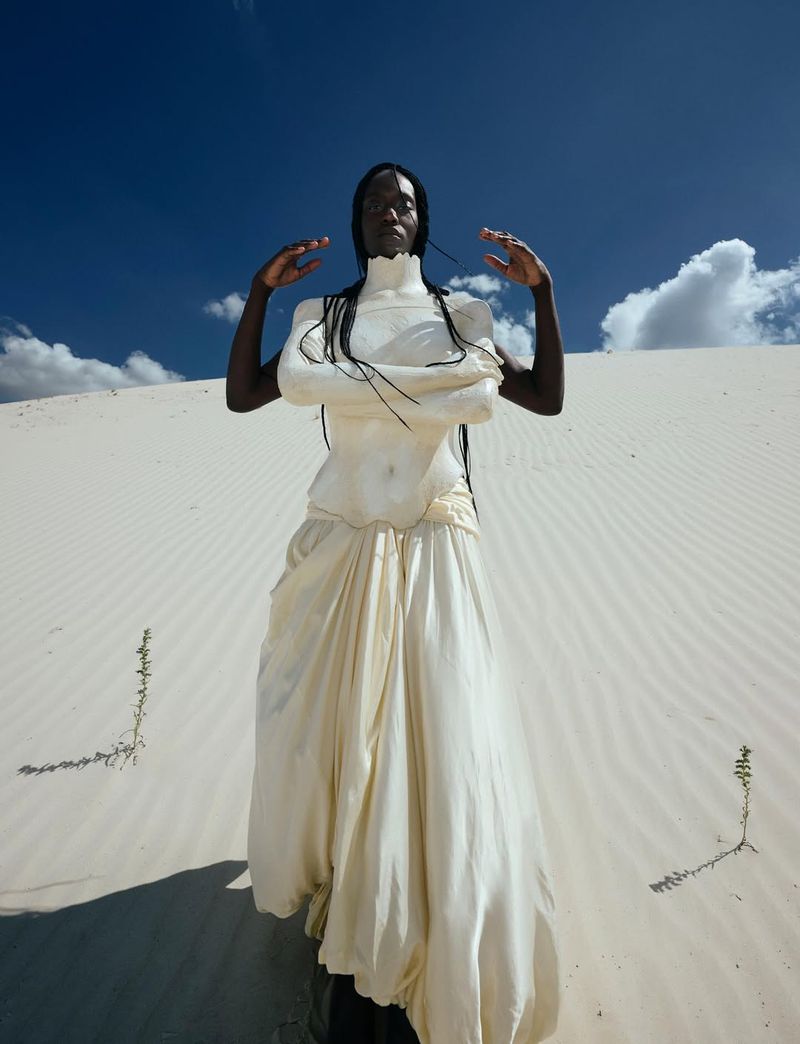 Woman in a white dress posing in a desert with a blue sky. Fashion shot with an outdoor setting and natural lighting.