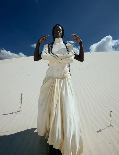 Woman in a white dress posing in a desert with a blue sky. Fashion shot with an outdoor setting and natural lighting.