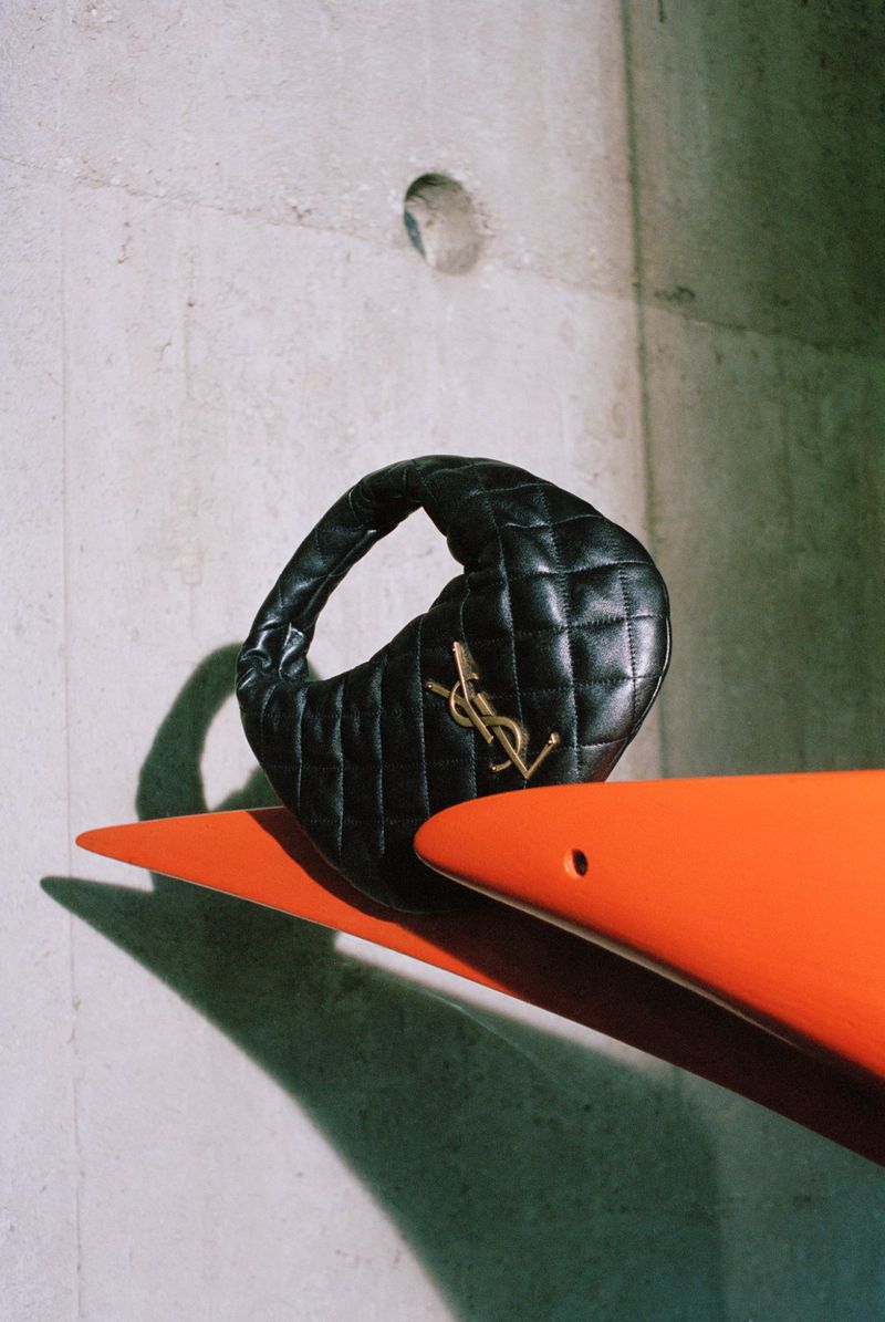 Black leather YSL hobo bag with gold hardware on an orange sculptural stand against a concrete wall background.