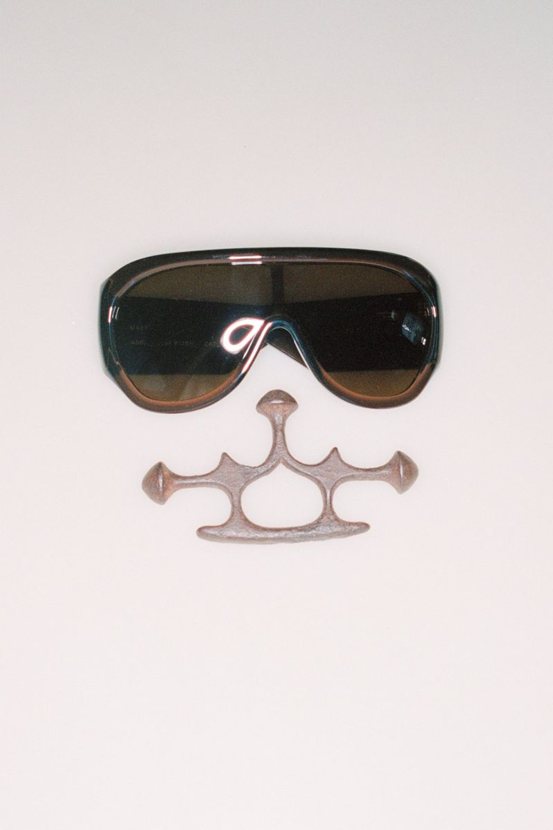 Sunglasses and brass knuckles on a white background, product photography of fashion accessories with dark colors and neutral studio setting.