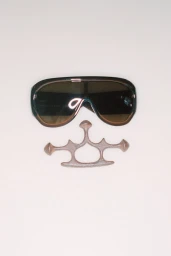 Oversized black visor sunglasses placed above a sculptural metal knuckle accessory on a pale background.