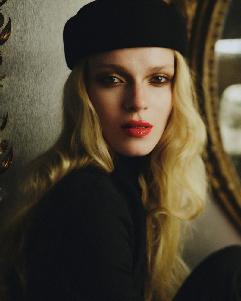 Portrait of a fair-skinned woman wearing a black beret and turtleneck sweater, accentuated by her blonde hair and bright red lipstick.