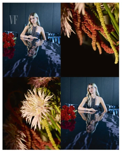 Blonde woman poses at a reflective black marble table with red roses and assorted greenery, illuminated by studio lighting.