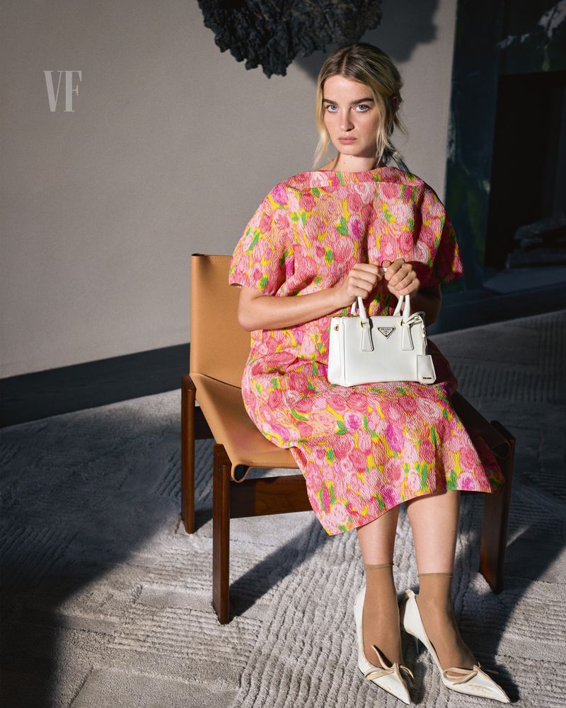 Model Adèle Farine seated in a tan chair wearing a pink floral dress and holding a white handbag for Vanity Fair Italia.