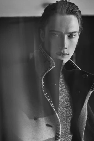 Black and white portrait of male model Freek Iven wearing a whipstitched collar coat over a sparkling turtleneck.