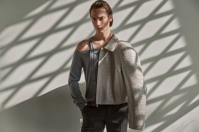 Male model in grey top and textured jacket posing against a wall with diagonal shadow patterns for Esquire Spain
