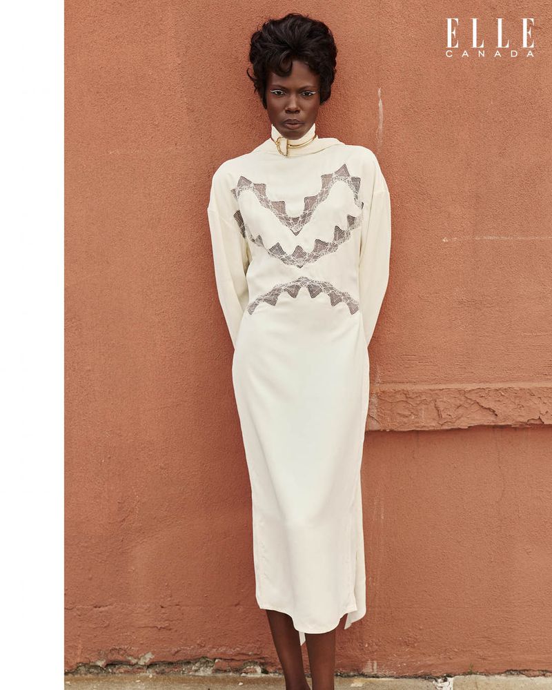 A woman in a white dress stands against a textured orange wall. The photo is a fashion editorial with a logo for Elle Canada.