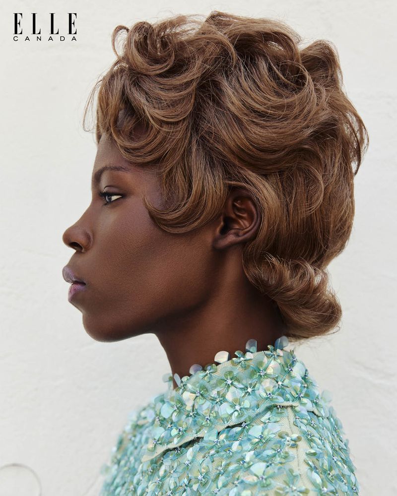 Profile portrait of an adult woman with brown wavy hair wearing a light blue beaded top, captured in a beauty fashion editorial style.