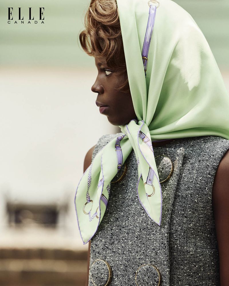 Portrait of an African-American woman wearing a printed headscarf and a grey jacket with large gold buttons, looking off to the side.