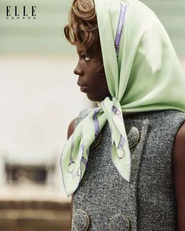Portrait of an African-American woman wearing a printed headscarf and a grey jacket with large gold buttons, looking off to the side.