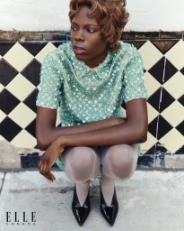 Model Agel Akol crouches in a mint green sequin dress and black patent heels against a diamond-tiled wall for Elle Canada.