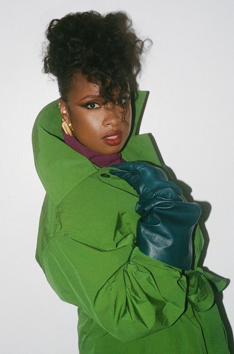 Close-up of an African-American woman in a lime-green puffer coat with dark-teal gloves, shot in a photo studio against a white backdrop.