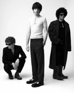 Three male models in dark sunglasses and tailored clothing posing against a plain white studio background.