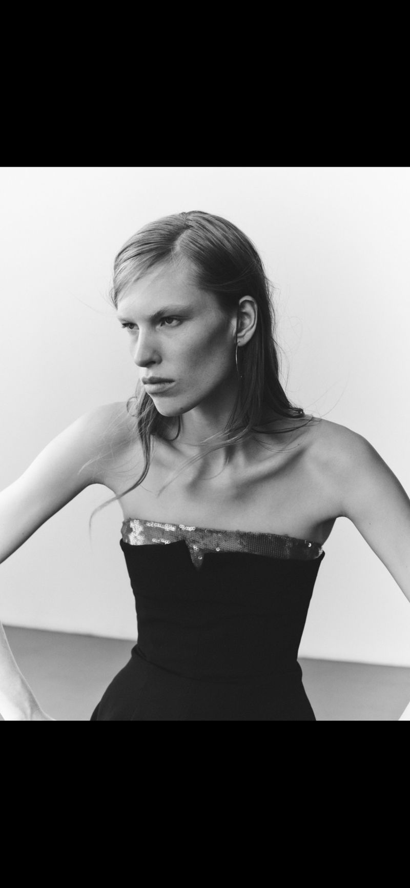 Portrait of an adult female with straight blonde hair wearing a strapless black dress, shot in black and white with a neutral expression.