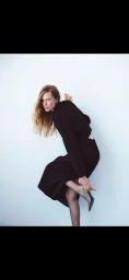 Model Leanne De Haan wearing a black long-sleeve dress and pointed mules against a plain white wall.