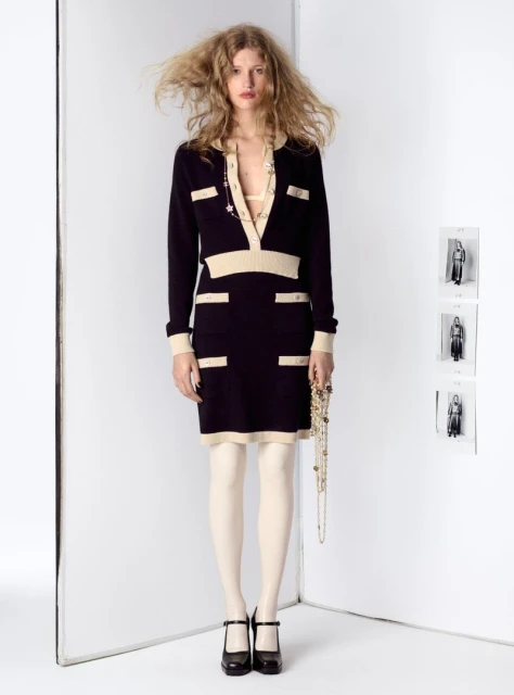 Woman poses in a black and beige collared dress with stockings and Mary Jane shoes in a white corner studio fashion shot.