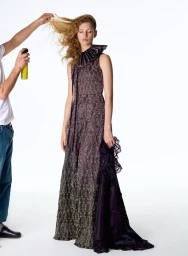 Model Apolline Rocco Fohrer in an intricate ruffled maxi gown having her hair sprayed on a white studio backdrop.