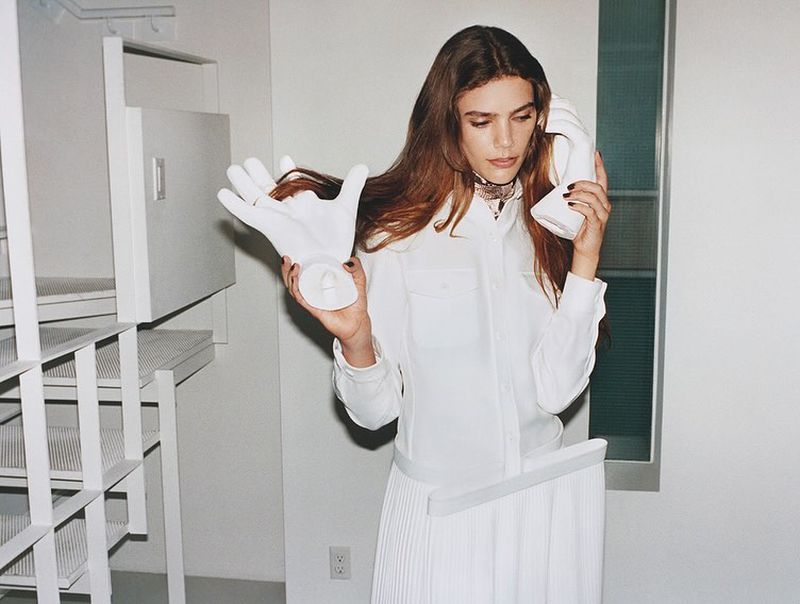 Adult female in a white skirt and shirt, holding a white telephone to her ear and a mannequin hand. Indoor photo studio setting.