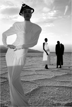 Monochrome fashion editorial image of models posing on a salt flat under a cloudy sky.