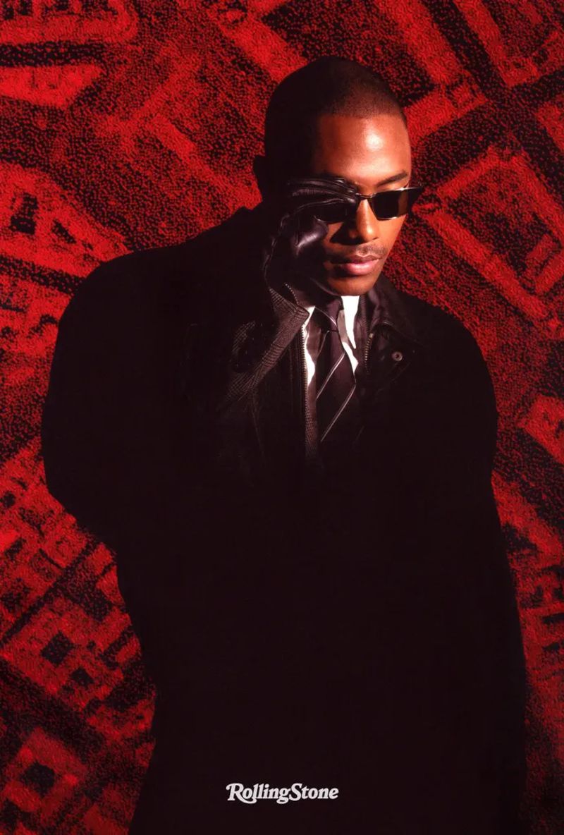 Portrait of an African-American male in a dark suit and sunglasses, set against a textured red and black background. Rolling Stone logo visible.
