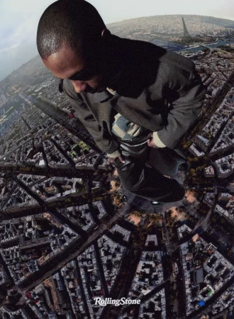 Aerial shot featuring an African American man in dark coat over a cityscape, highlighting architectural details and an urban landscape.