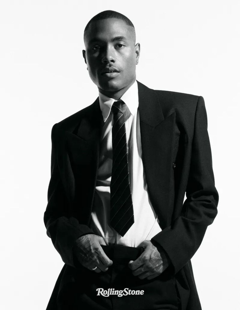 Portrait of an adult male in a black suit and tie against a white background, captured in a studio setting for Rolling Stone.