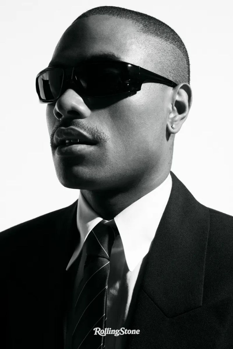A stylish Black man in a suit and sunglasses poses against a bright white background for a striking Rolling Stone portrait.