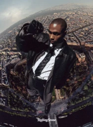 Steve Lacy wearing a black leather jacket and striped tie looking down from above an aerial city view for Rolling Stone.