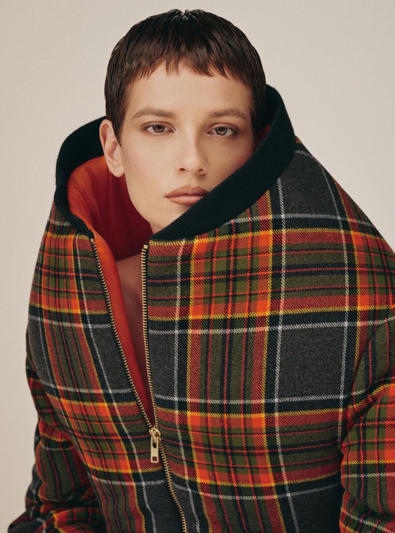 Close-up of a person wearing a colorful plaid jacket with a zipper in a photo studio with a light background.