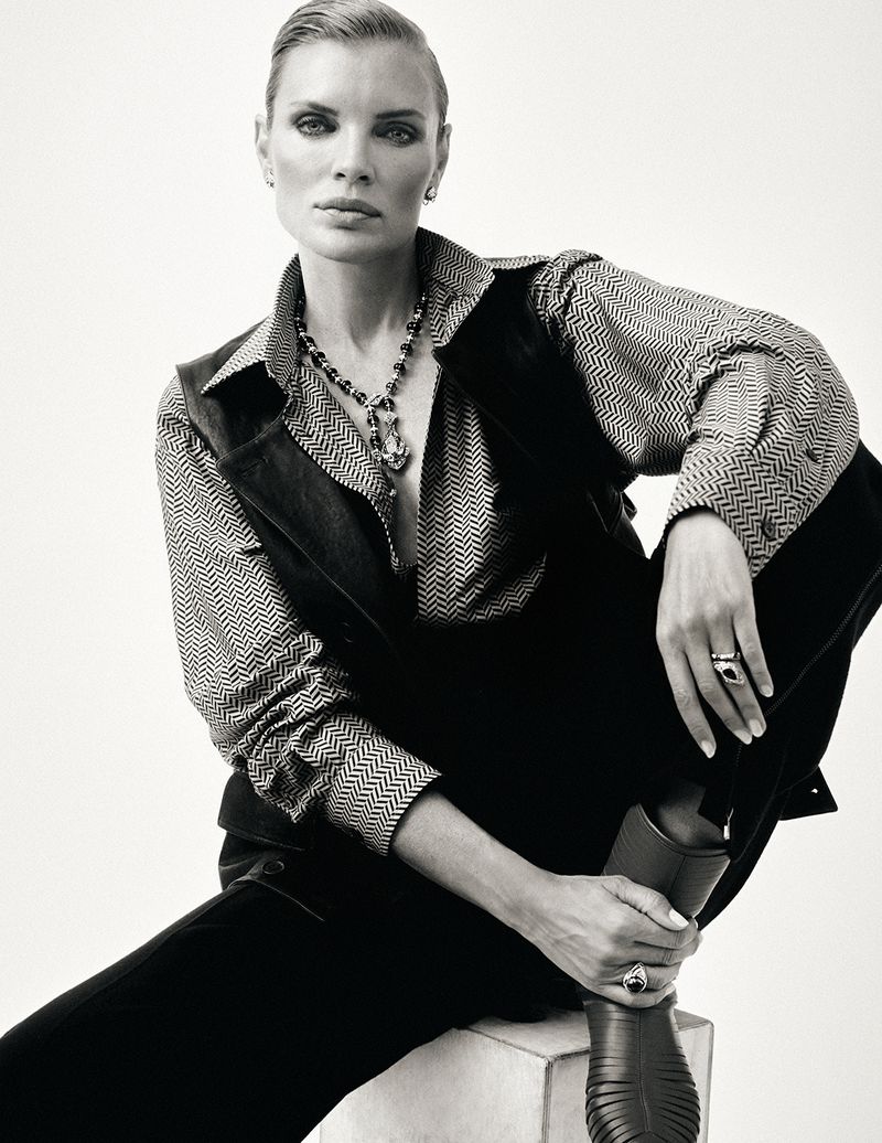 Model Esther Cañadas seated in a patterned button-down shirt and black vest against a plain white studio background.