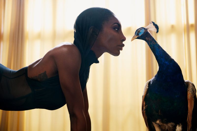 Woman in sportswear facing a peacock in an indoor setting with natural lighting and a shallow depth of field, creating an intimate and captivating image.