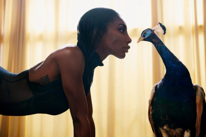 Woman in sportswear facing a peacock in an indoor setting with natural lighting and a shallow depth of field, creating an intimate and captivating image.
