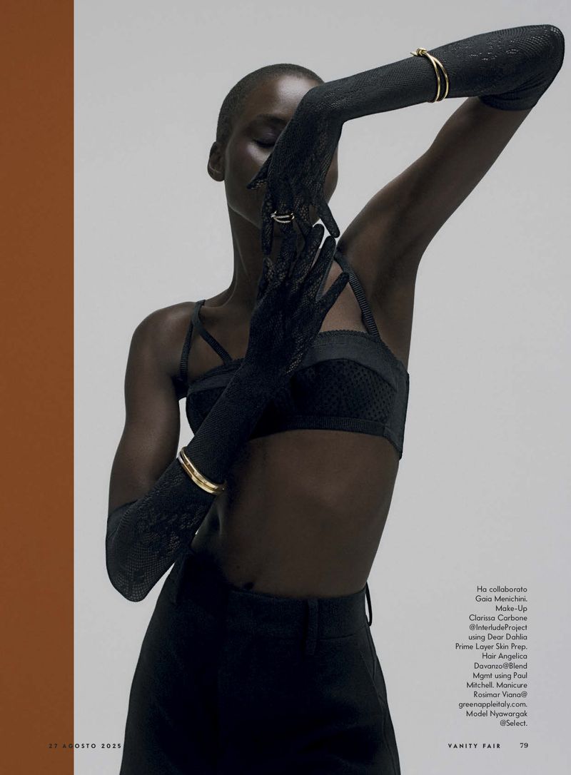 A striking fashion shot featuring a slender Black woman in black attire, gloves, and gold jewelry, posing against a gradient background.