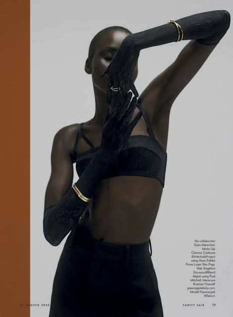 A striking fashion shot featuring a slender Black woman in black attire, gloves, and gold jewelry, posing against a gradient background.