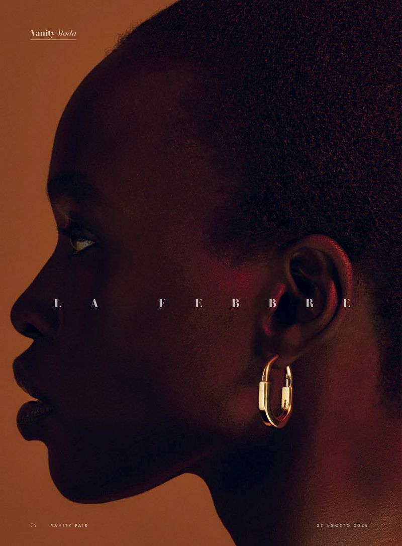 Portrait of an African woman in profile wearing a gold earring with dark hair against a warm background for Vanity Moda magazine.